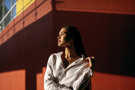 Young hispanic woman in white shirt against red and yellow wall in sunlight.の写真素材