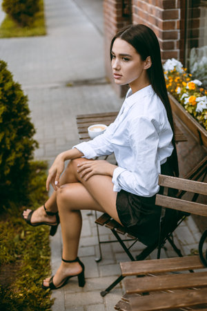 Caucasian young female in white shirt sitting at outdoor cafe table.の写真素材