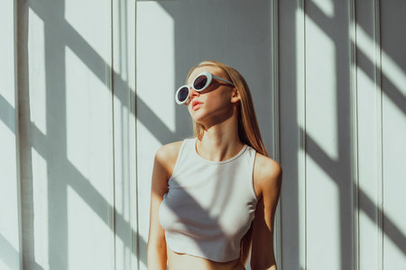 Caucasian young female in sunglasses posing against sunlit wall.の写真素材