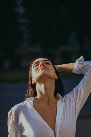 Young caucasian female in white shirt posing outdoors in sunlight.の写真素材