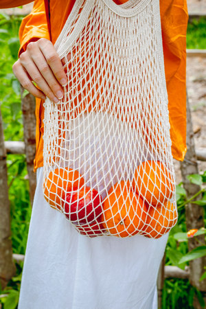Person with mesh bag holding fresh oranges and apples.の写真素材