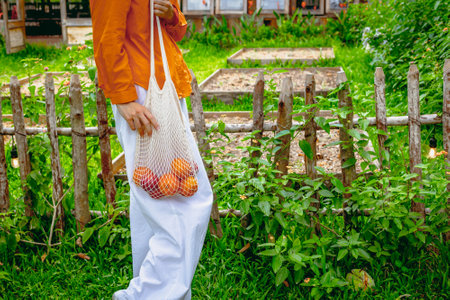 Young adult caucasian female with reusable bag of apples in garden setting.