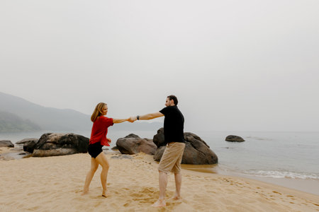 Caucasian couple dancing on beach with rocks in background.の写真素材