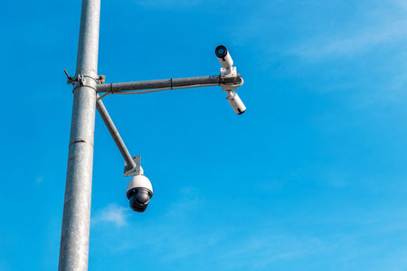 Security cameras mounted on pole against clear blue sky for surveillance.の写真素材