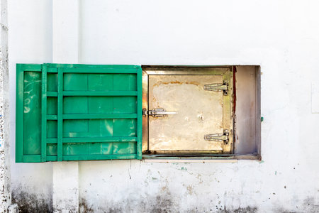 Closed green and metallic hatch on weathered white wall.の写真素材
