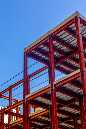 Red steel beam building frame against clear blue sky.の写真素材