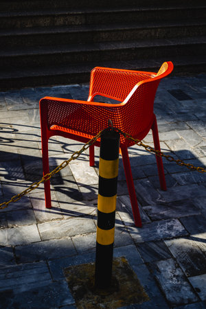Red chair on stone pavement in sunlight near black and yellow post.の写真素材