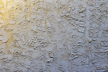 Textured white plaster wall with abstract patterns and yellow tint.の写真素材