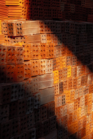 Stacked red clay bricks in sunlight with shadows highlighting textured surfaces.