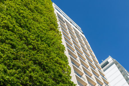 Green facade on modern urban building against clear blue sky.の写真素材