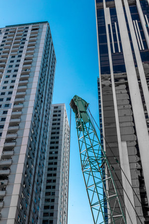 Urban construction scene with crane and skyscrapers against blue sky.の写真素材