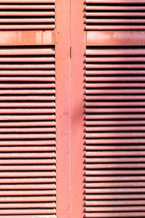 Pink louvered shutters with horizontal slats on sunlit exterior.の写真素材