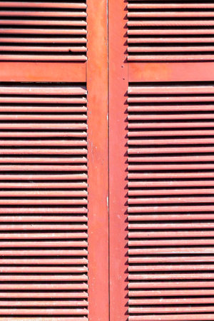 Red wooden shutter with horizontal slats in bright sunlight.の写真素材