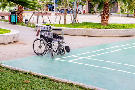 Empty wheelchair on outdoor sports court surrounded by trees and grass.の写真素材