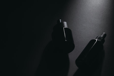 Minimalist dark dropper bottles on black background with dramatic lighting.の写真素材