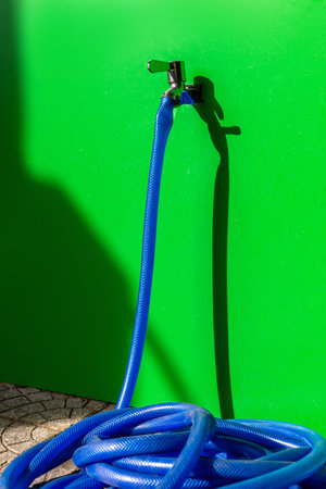 Blue garden hose coiled on green wall with shadow in sunlight.の写真素材