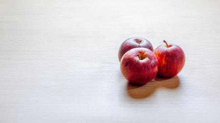 Three red apples on light wooden surface with minimalist design.の写真素材