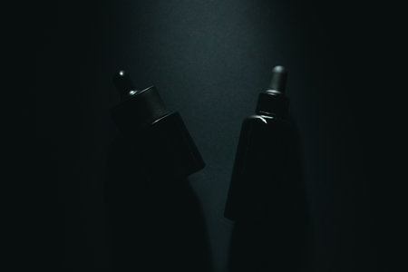Minimalist dark skincare bottles with pipettes on black background.の写真素材