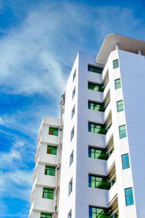 Modern white apartment building with green windows against blue sky.の写真素材