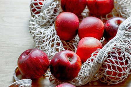 Fresh red apples in eco-friendly reusable mesh bag on wooden surface.の写真素材
