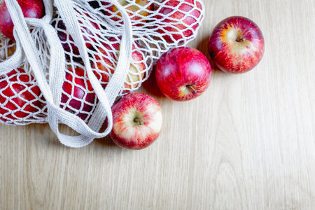 Red apples in net bag on wooden surface evoking freshness and simplicity.