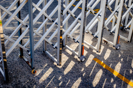 Metallic expandable gate with wheels casting shadows on asphalt surface.