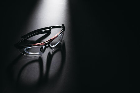 Stylish modern eyeglasses on dark reflective surface under spotlight.