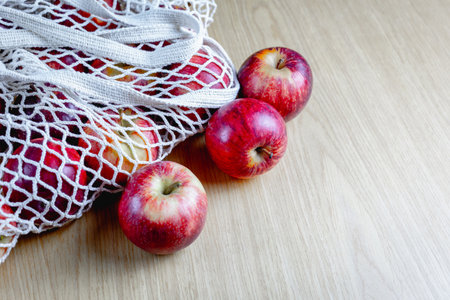 Fresh red apples in reusable mesh bag on wooden surface.の写真素材