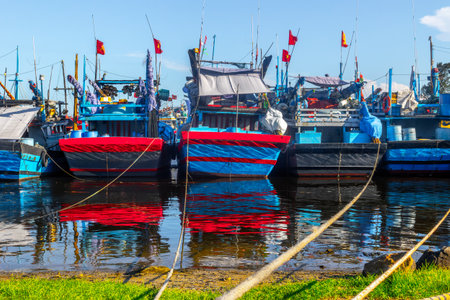 Colorful fishing boats with reflections anchored in harbor on a sunny day.