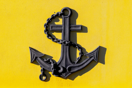 Black anchor with cross design on bright yellow background.