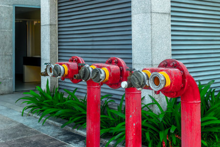 Red fire hydrant valves outside building with metal shutters and green plants.