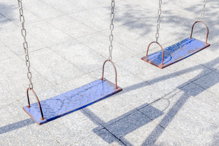 Empty metal swings hanging on chains in a sunny playground.の写真素材