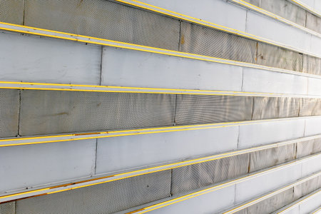 Industrial metal wall with yellow stripes and mesh panels close-up.の写真素材