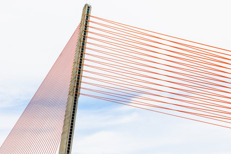 Modern cable-stayed bridge with red suspension cables against blue sky.