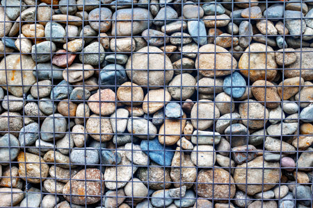 Assorted river stones behind wire mesh fence for garden landscaping.の写真素材