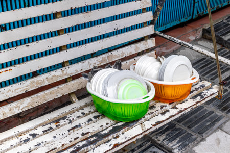 Two plastic basins with clean dishes on white wooden bench outdoors.の写真素材