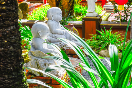 Two stone monk statues in lush garden with greenery and red lanterns.の写真素材