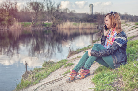 young girl talking to mobile phone in the park near the lakeの写真素材