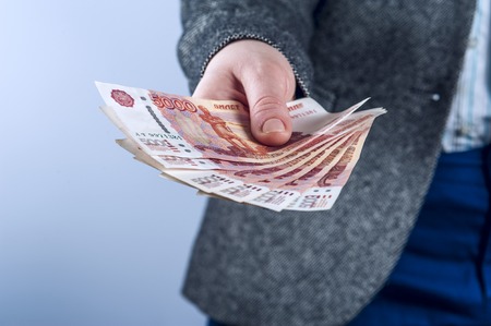 Businesswoman in a suit holds Russian rubles on a grey background.