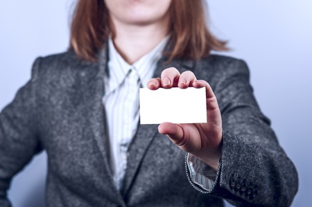 Young woman  in grey suit holds business card on grey background. Focus on card and fingers. Horizontal view.の写真素材