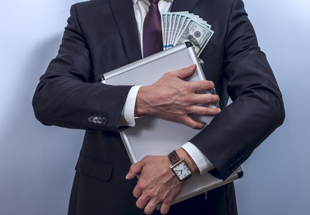 Man in suit holds metal briefcase with dollars on grey background.  Conception of safe storage and protection of cash. Financial theme. Horizontal view.の写真素材