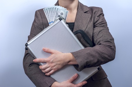 Woman in suit holds metal briefcase with dollars on grey background.  Conception of safe storage and protection of cash. Financial theme. Horizontal view.の写真素材