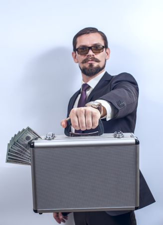 Man in suit with eyeglasses holding a suitcase with US dollars. Financial theme.  Focus on suitcase....