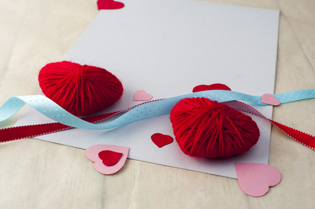 Two red knitted hearts, ribbons and white sheet with paper hearts. Valentine's theme. Vertical view.の写真素材