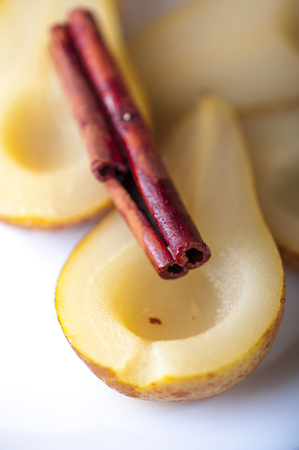 Closeup of Pears cooked in sugar syrup with cinnamon stick on white plateの写真素材