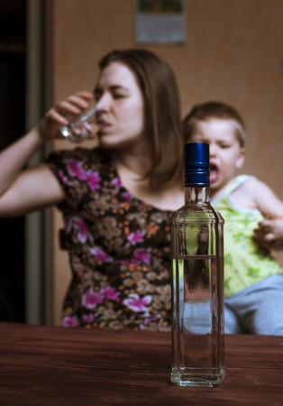 Drunk woman with alcoholic drink and crying child. Female alcoholism. Focus on bottle.の写真素材