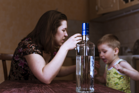 Quarrel between drunk mother and her little son. Family problems, female alcoholism. Focus on bottle.の写真素材