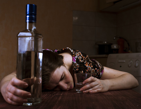 Tired drunk woman sleeping on the table and holding her glass. Focus on hand with glass.の写真素材