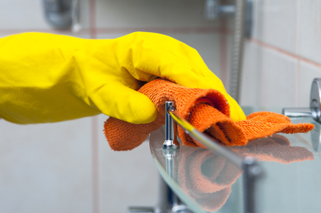 Closeup of woman's hand in yellow glove cleaning bath shelf. Cleaning concept.の写真素材
