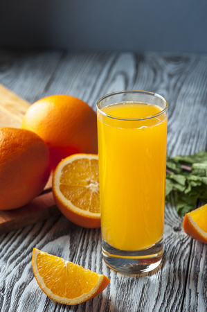 Glass of fresh orange juice, slices of orange and mint leaves on wooden table. Focus on orange slice.の写真素材